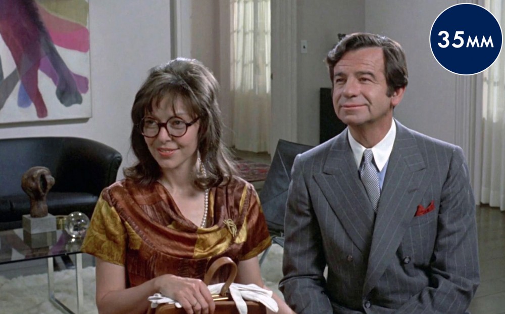 Actors Walter Matthau and Elaine May sit together in a living room.