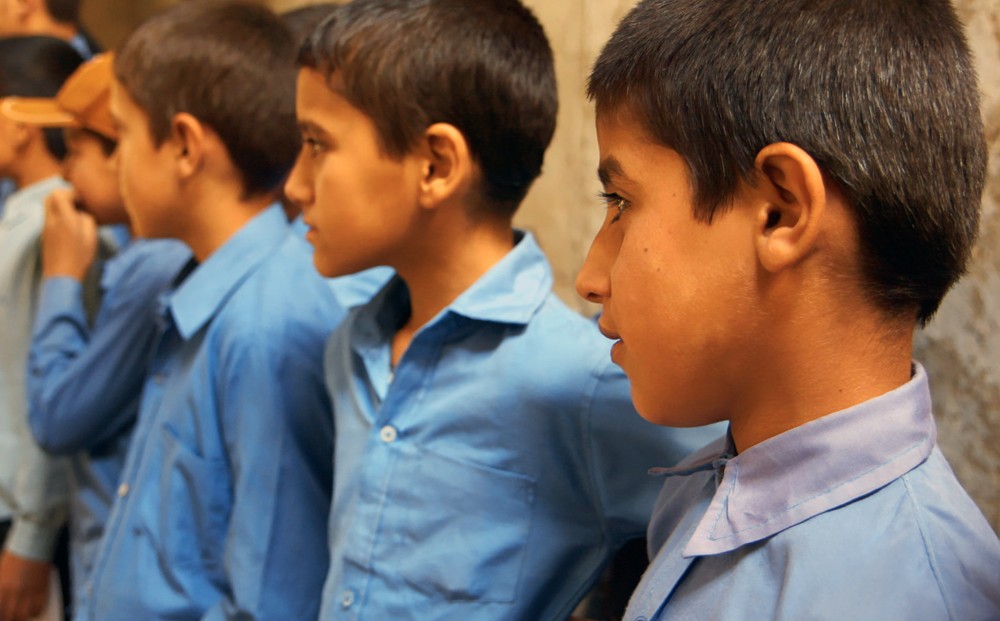School children in blue shirts stand in a line.