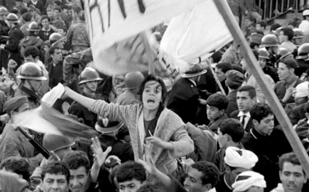 Still from THE BATTLE OF ALGIERS - A woman shouts and waves fabric in the middle of a crowd of civilians and soldiers.