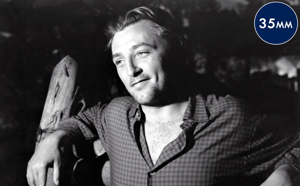 Actor Robert Mitchum leans against a wooden fence.