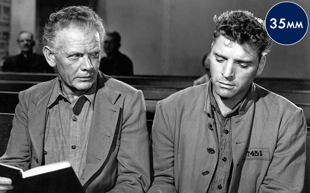 Actor Burt Lancaster sits next to another man in church pews.