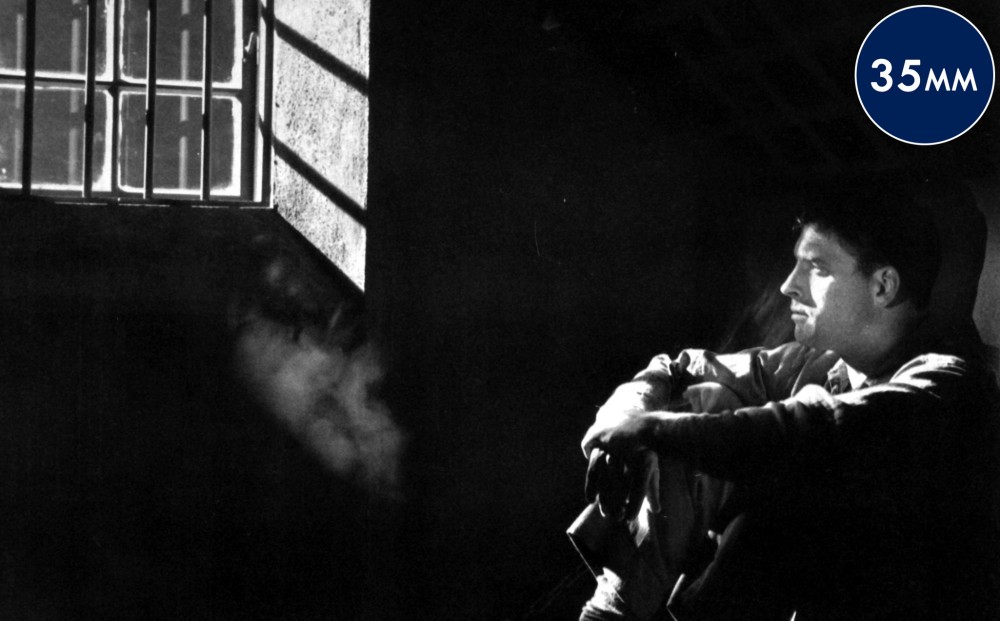 Actor Burt Lancaster sits in profile in a dark prison cell.
