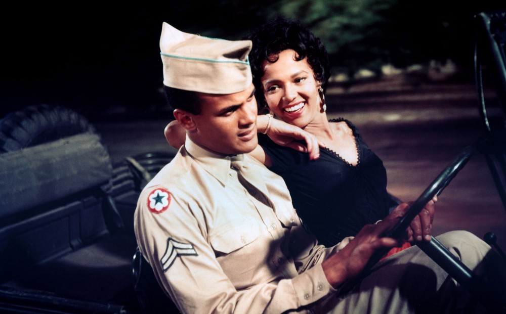 Actors Dorothy Dandridge and Harry Belafonte sit in a car together; he wears a soldier's uniform.