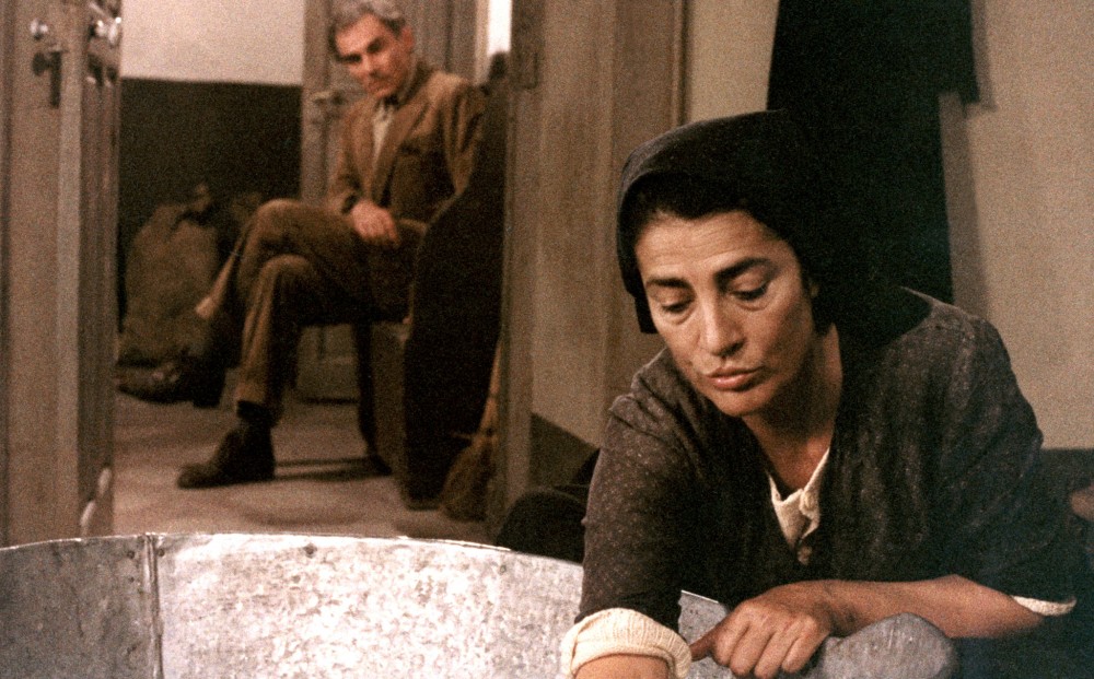 Actors Gian Maria Volontè and Irene Papas; he looks on as she scrubs a basin.