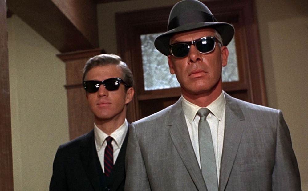 Actors Lee Marvin and Clu Gulager wear suits, ties, hats, and sunglasses. 