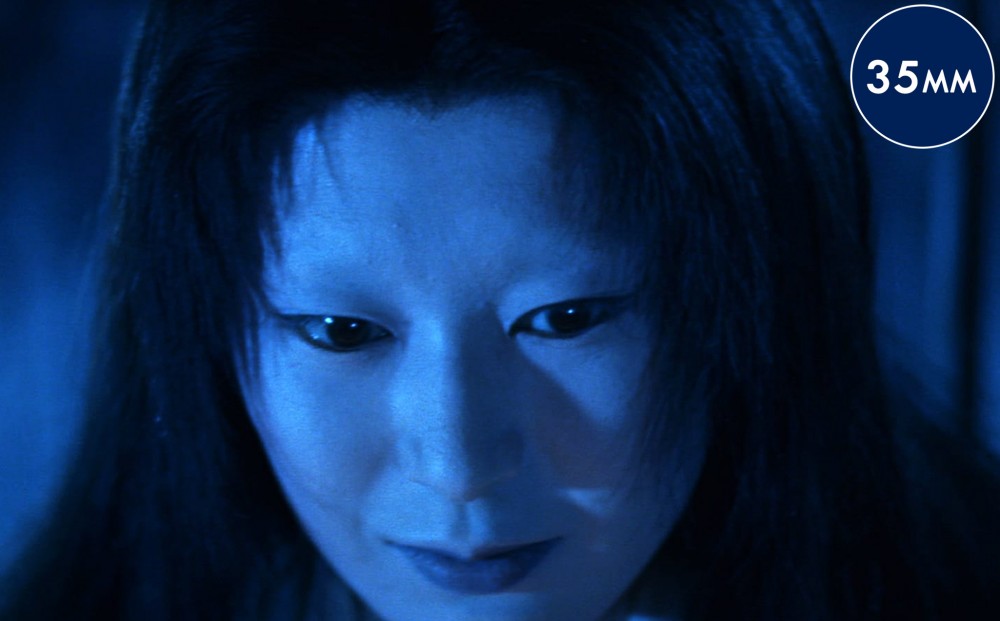 Close-up on a woman's face; she is pale and lit with a blue light.