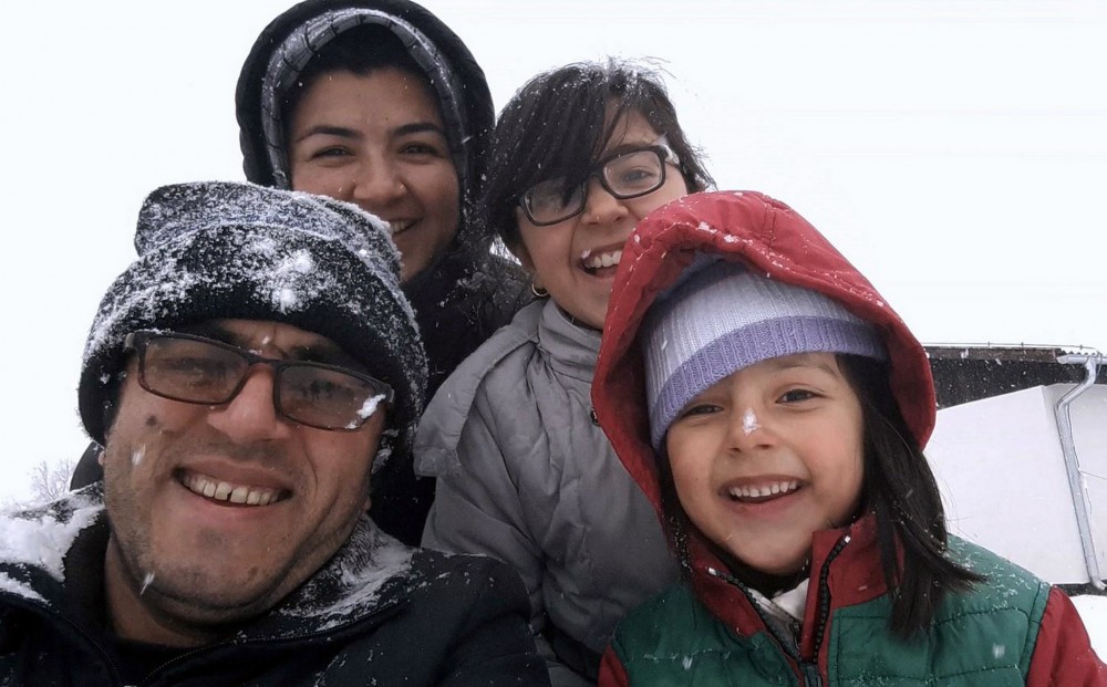 A family wearing winter clothing, dusted with snow, smiles at the camera for a selfie.