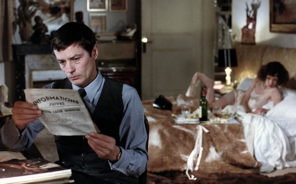 Actor Alain Delon reads a newspaper with the headline 