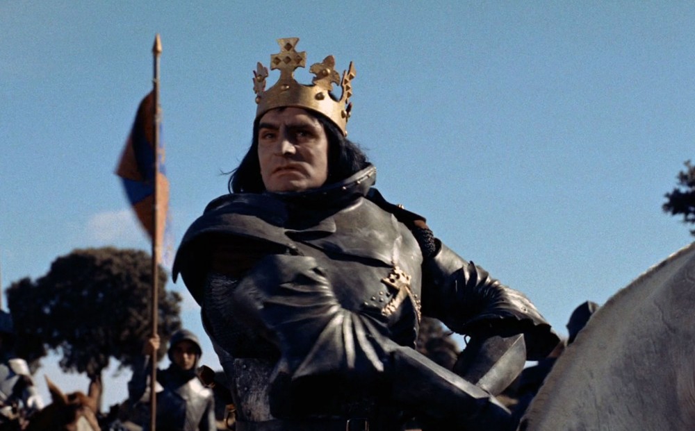 Actor Laurence Olivier astride a horse, wearing a crown.