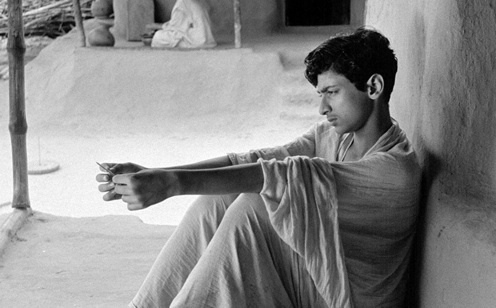 An adolescent Apu, actor Smaran Ghosal, sits while gazing off.