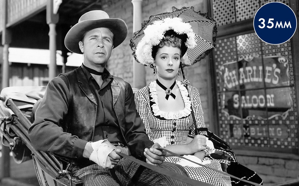 Actors Dick Powell and Jane Greer sit on a carriage.
