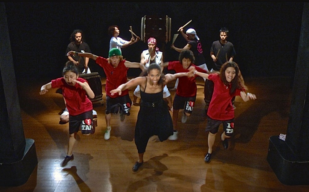 From TAP WORLD - Five tap dancers perform on a stage, with five musicians playing taiko and other drums in the back.