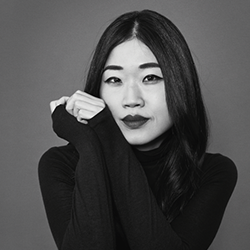 mary hk choi headshot – mary poses with hands on her face in black turtleneck