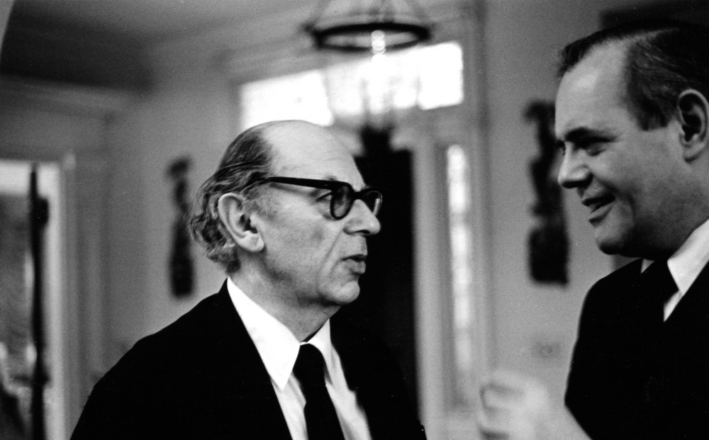 Black and white image of two men in suits talking.