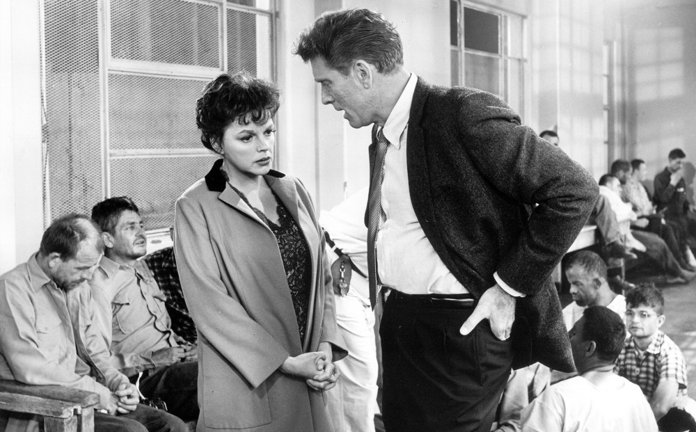 Actor Burt Lancaster speaks with Judy Garland in a room where children and adolescents sit around.
