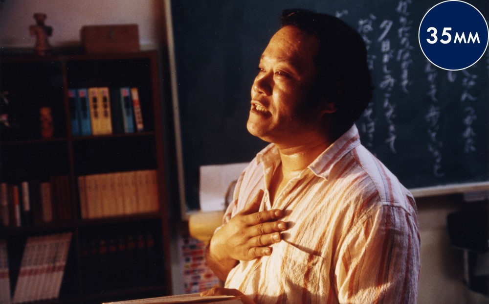 A man in front of a chalkboard stands with his hand over his heart.