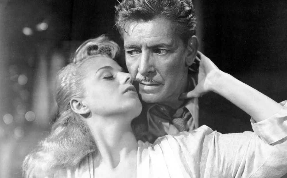 Actor Shelley Winters holds actor Ronald Colman's head, about to kiss him.