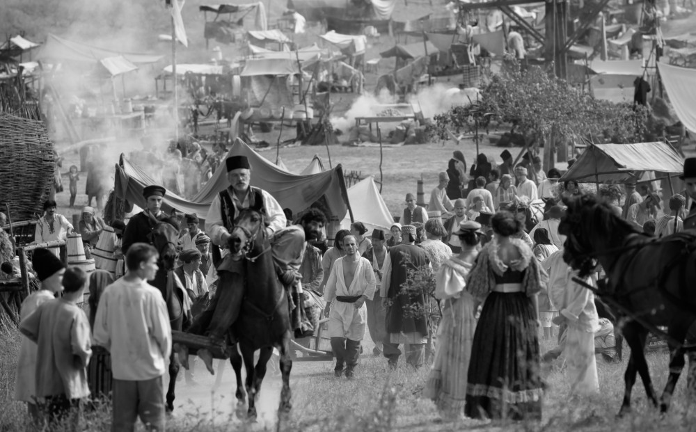 Black and white image of what looks like a gypsy encampment, with many people, some horses, and a variety of make-shift shelters.