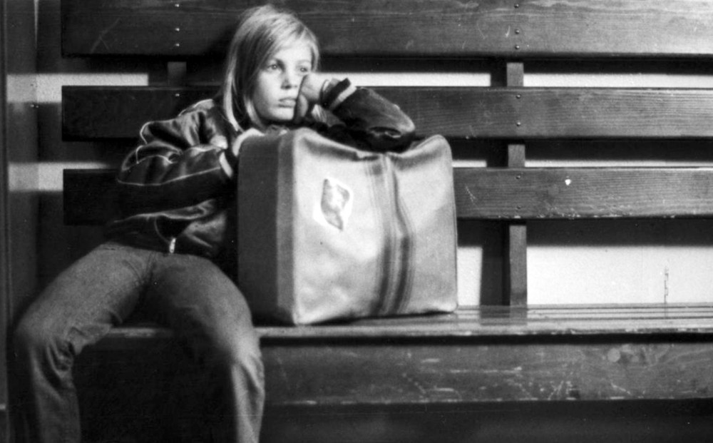 Actress Yella Rottländer sits on a bench and leans on her luggage.