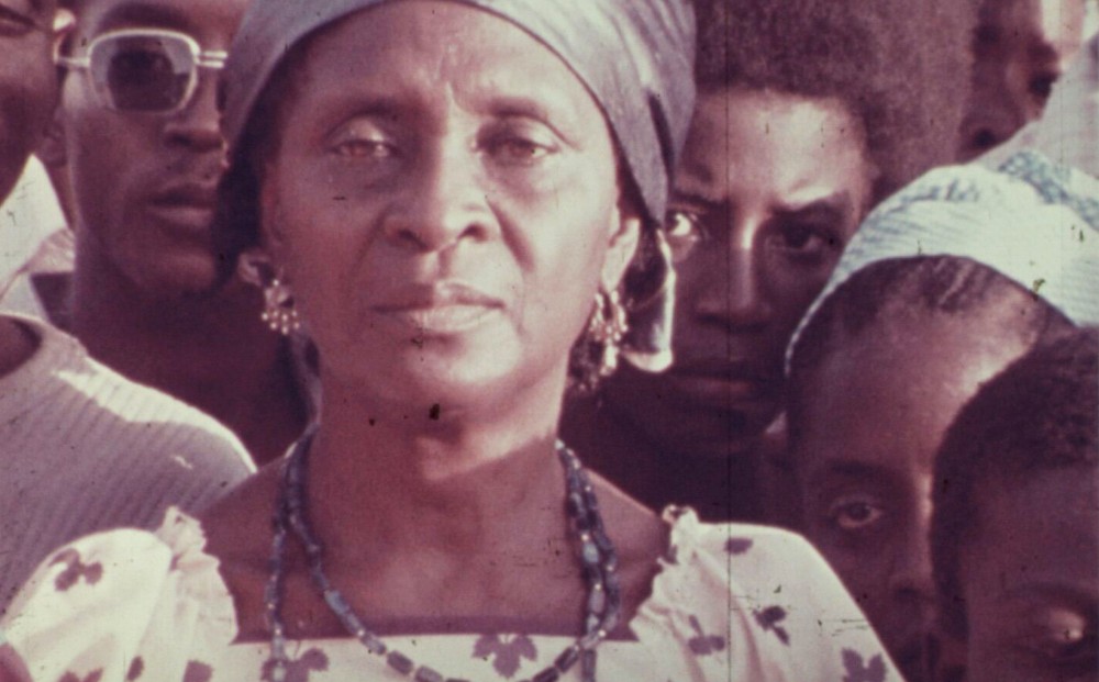 An older woman stands in a crowd of other people.