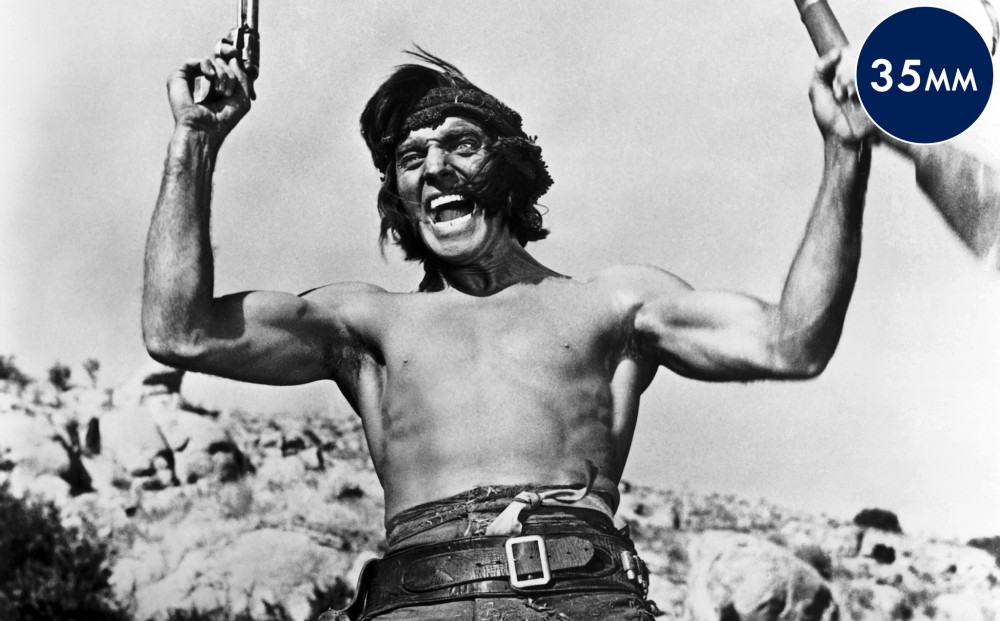 A shirtless Burt Lancaster wields two guns, one in each hand.