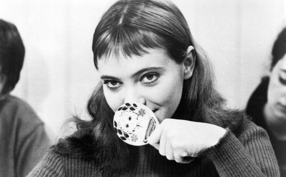 Actor Anna Karina smiles softly, with her mouth slightly covered.