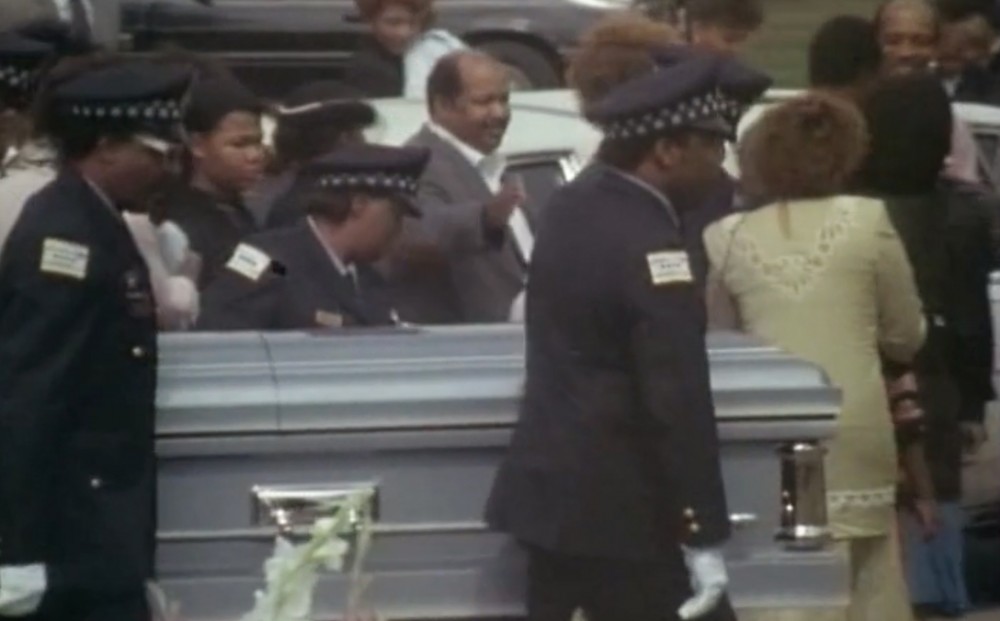 Officers carry a casket, surrounded by funeral-goers.