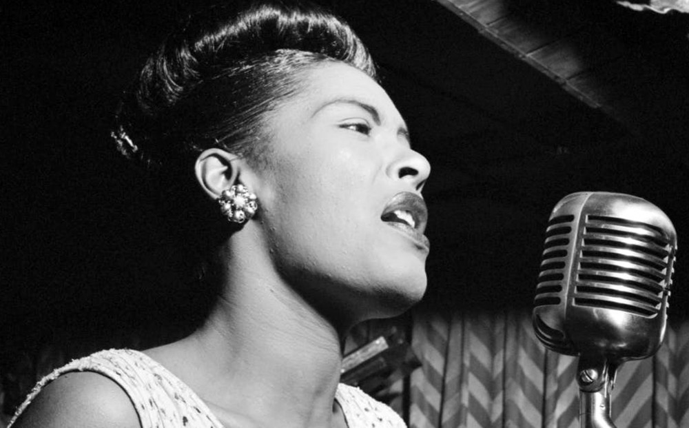 Black and white image of Billie Holiday sings in front of a microphone.