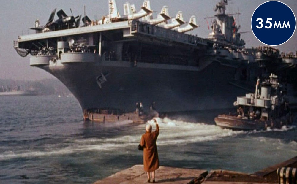 A woman stands at a dock as a large ship sails away.