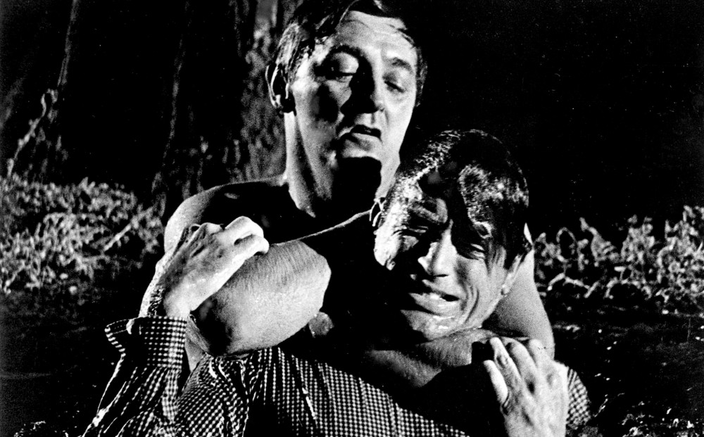 Actor Robert Mitchum holds Gregory Peck tightly around the neck; they are locked in struggle and both wet.