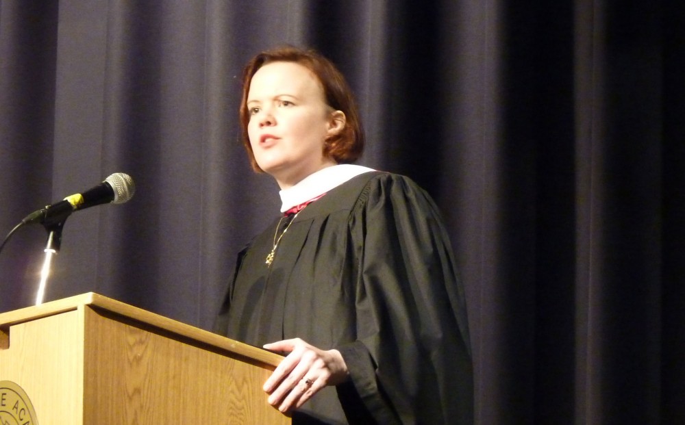 Caraid O'Brien stands at a lectern in graduation robes.