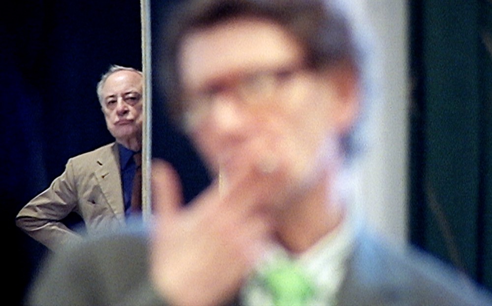 An out-of-focus Yves Saint-Laurent in the foreground; Pierre Bergé looms in the background.