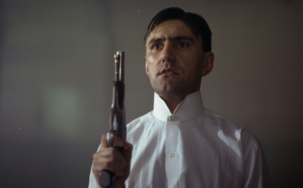 A man holds a gun, pointed towards the ceiling.