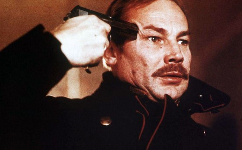 Actor Klaus Maria Brandauer holds a gun to his own forehead.
