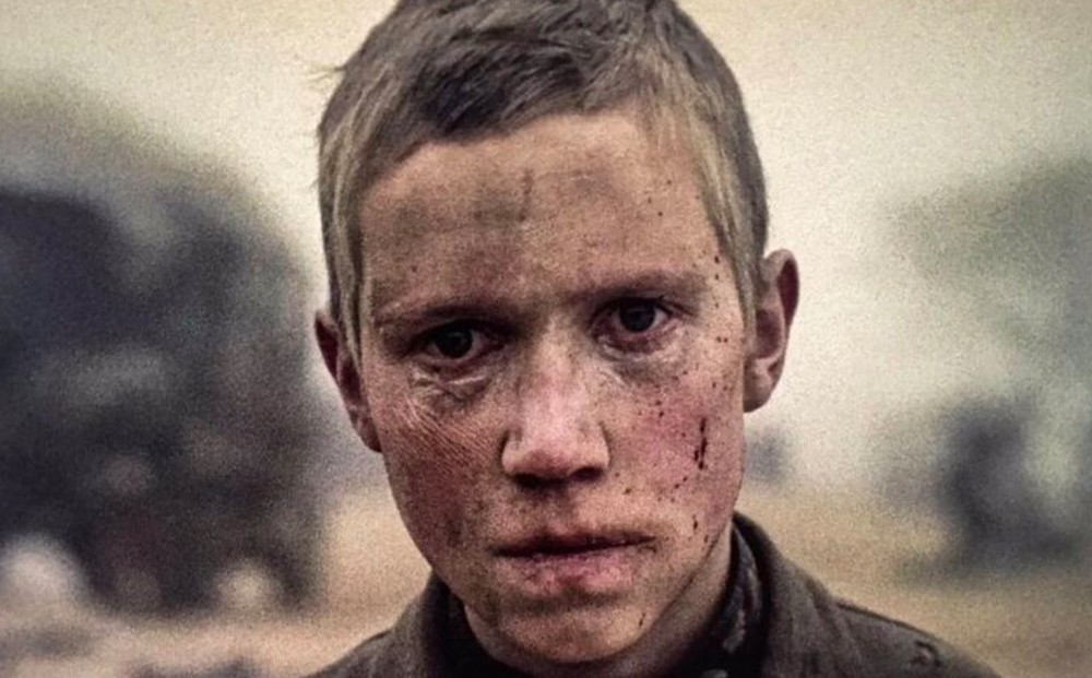 Close-up on the face of a young boy, covered in dirt and some blood.