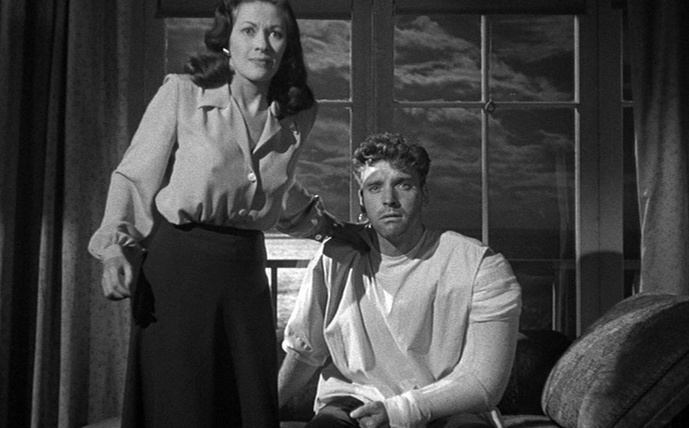 Actor Burt Lancaster has a cast on one arm; Yvonne De Carlo stands beside him with her arm on his shoulder.