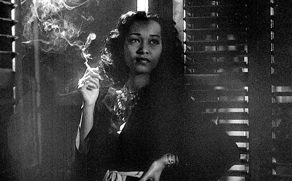 A woman leans against a window sill and smokes a cigarette.