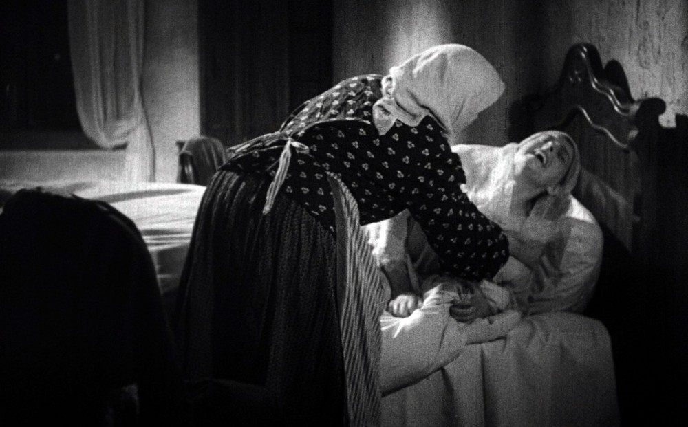 A woman writhes in bed, tended to by a maid.