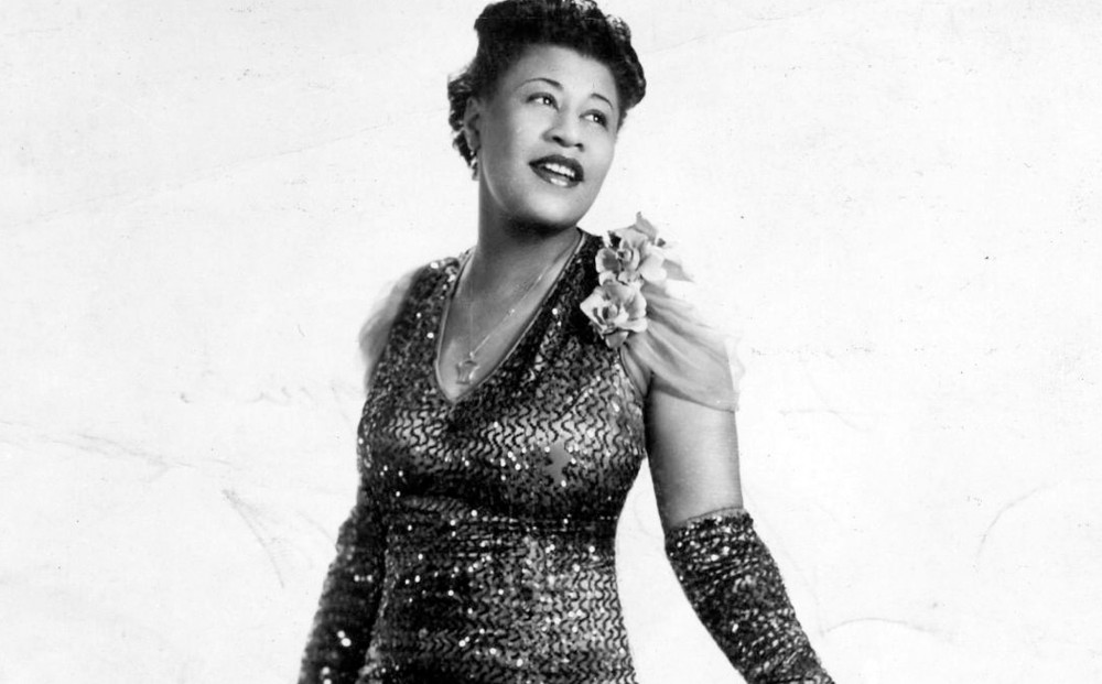 Ella Fitzgerald sings, wearing a sequined evening gown with gloves.