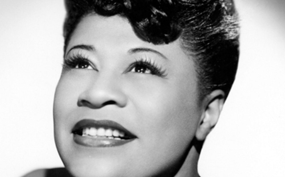 Close-up on Ella Fitzgerald, who smiles as she looks upwards.