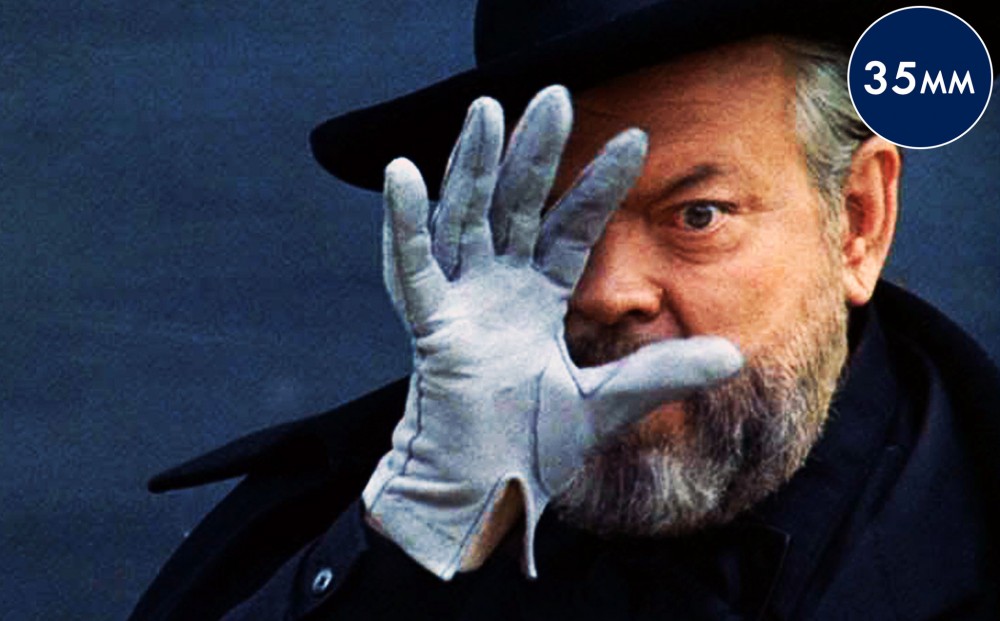 Actor/director Orson Welles holds a gloved hand up to his face.