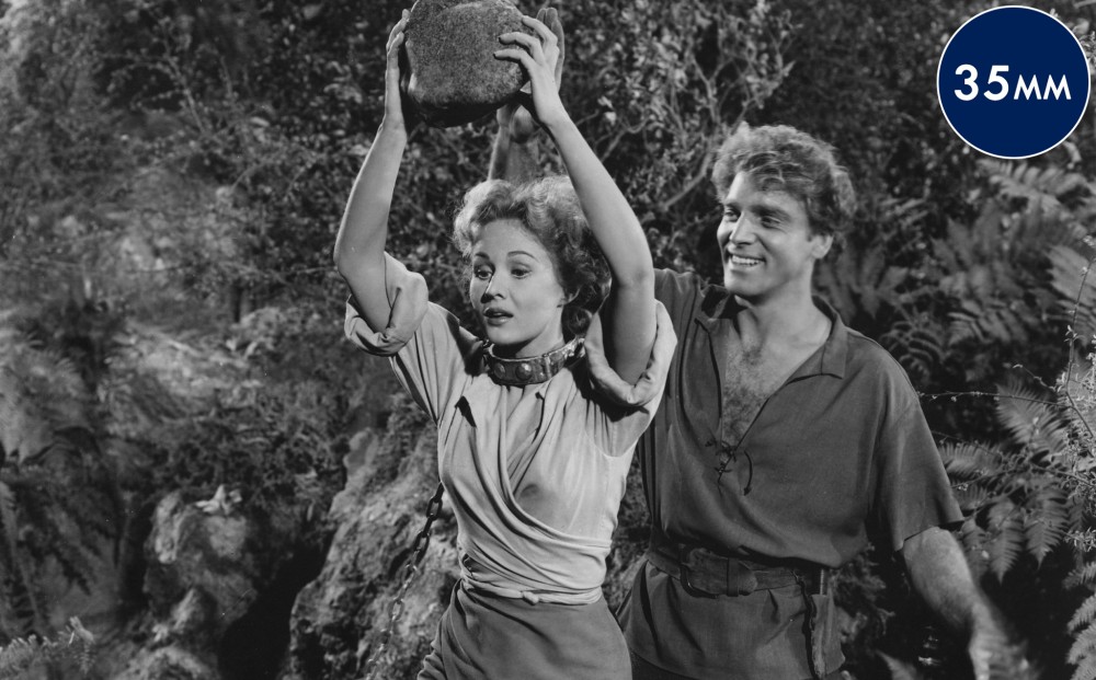 Actor Burt Lancaster stands behind Virginia Mayo; she holds a large rock over her head.