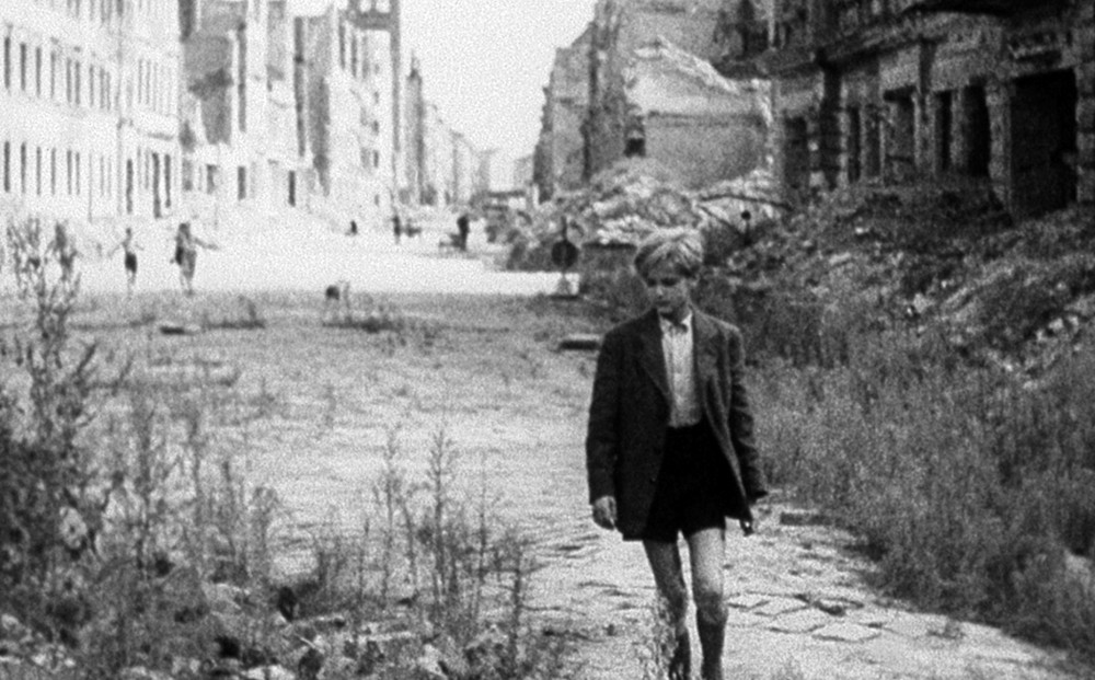 A young boy in a school uniform walks in a desolate urban street.