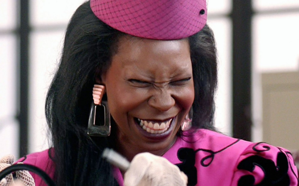 Whoopi Goldberg grins, wearing a bright pink outfit that includes a matching hat.