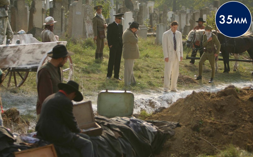 Workers, army officers in uniform, horses, and a man in a white suit are all present in a cemetery.