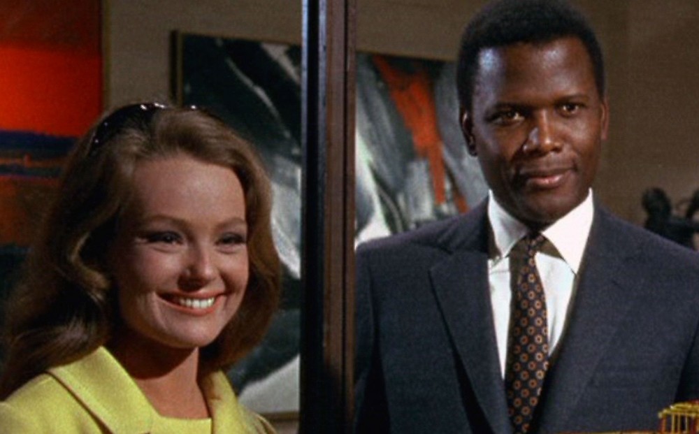 Actors Katharine Houghton and Sidney Poitier stand and smile in the same direction.