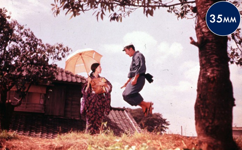 A man and a woman outside; the man is jumping and the woman is holding an umbrella.