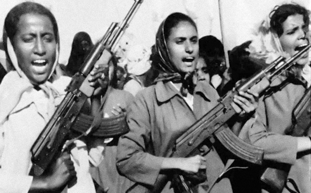 Three women wearing scarves over their heads, holding machine guns.