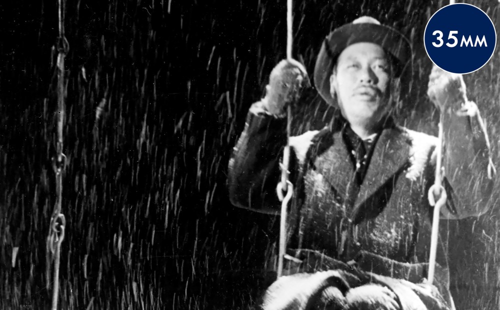 Actor Takashi Shimura man sits on a swing outside in the snow.