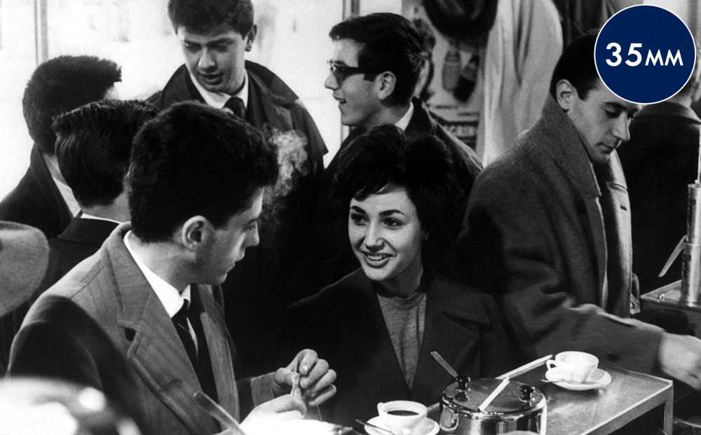 Two lead actors sit at a crowded cafe.